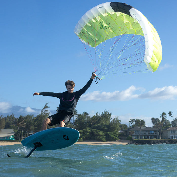 Jeffrey flying duotone stash parawing one-handed over water with a clear blue sky and beach in the background