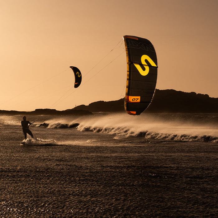Kitesurfer on a beach with Code NXT v2 sail during sunset.