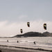 Three kite surfers with Code NXT v2 kites in the sky over a beach and ocean landscape.