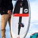 Person holding a white surfboard with red and black accents on a beach. with one front strap and rear Reedin Layflat foot strap