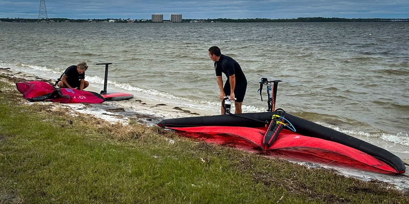 2 men setting up wing foil gear on the beach